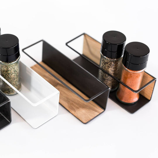 Spice rack organizer featuring a combination of white and black metal frames with wooden inserts, neatly holding spice jars in an organized arrangement.