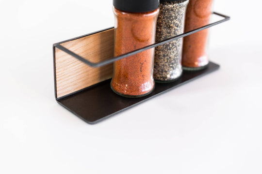 Spice rack with a black metal frame and a wooden back, holding three spice jars in a sleek, compact design.