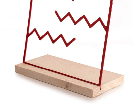 Red zigzag metal jewelry holder on a natural wood base, simple and minimalistic design.