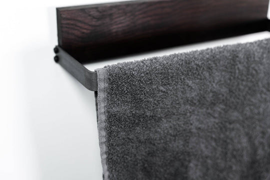 Sleek black metal towel rack with a textured dark wood base, holding a plush gray towel, showcasing a contemporary and refined design.