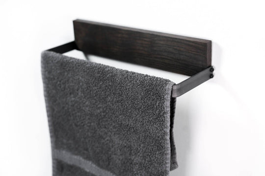 Black metal towel rack with a textured dark wooden backing, holding a soft gray towel with a visible fabric texture.