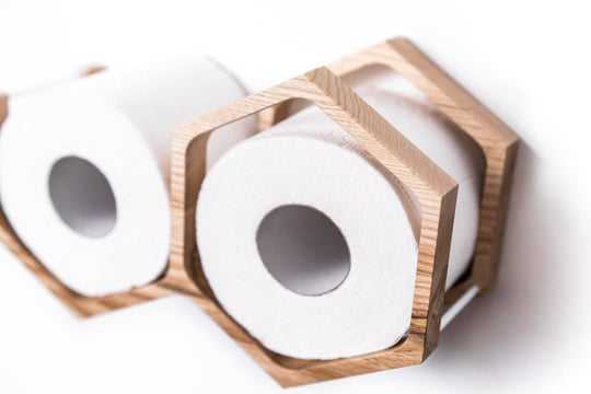 Close-up of a wall-mounted mini honeycomb toilet paper holder, displaying two rolls of toilet paper. The holder is crafted from textured wood with a natural finish and a geometric design.