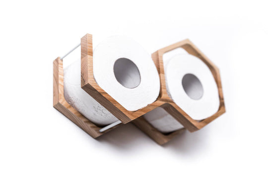 Close-up of a wall-mounted mini honeycomb toilet paper holder, displaying two rolls of toilet paper. The holder is crafted from textured wood with a natural finish and a geometric design
