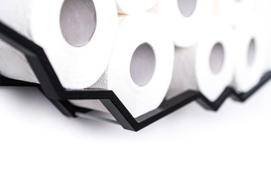 Close-up of a wall-mounted black zigzag toilet paper holder with a textured surface, displaying multiple rolls of toilet paper.